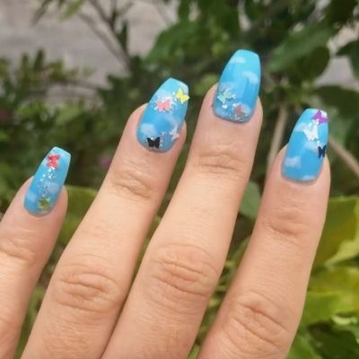 Hand of a person painted in a light blue color, adorned with an array of colorful butterflies delicately attached