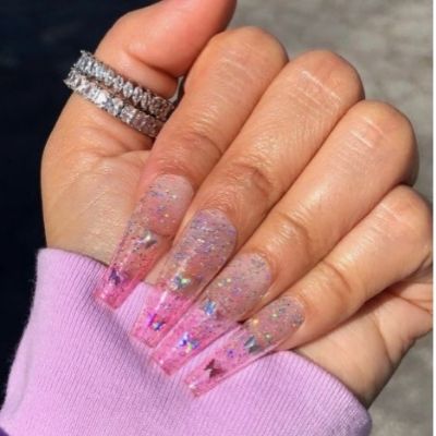 Hand of a person with long nails painted in a dazzling glitter nail polish, forming a captivating butterfly pattern