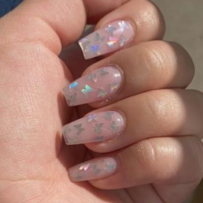 Hand of a person with nails painted in a light glitter nail polish, featuring butterfly stickers, creating a sparkling design