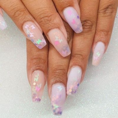 hand of a person's nails painted with pink color, adorned with butterfly confetti nail design