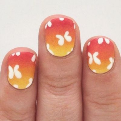 The hand of a person is adorned with a sunset-inspired butterfly nail design